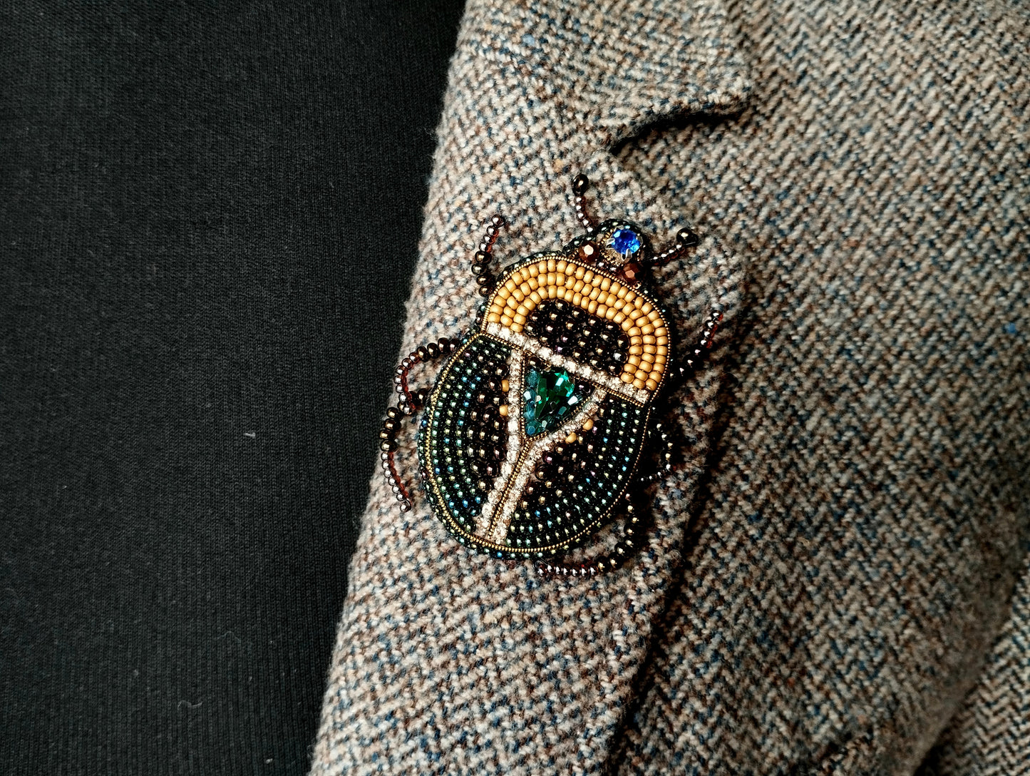 A close-up of a decorative insect brooch on a tweed jacket lapel.