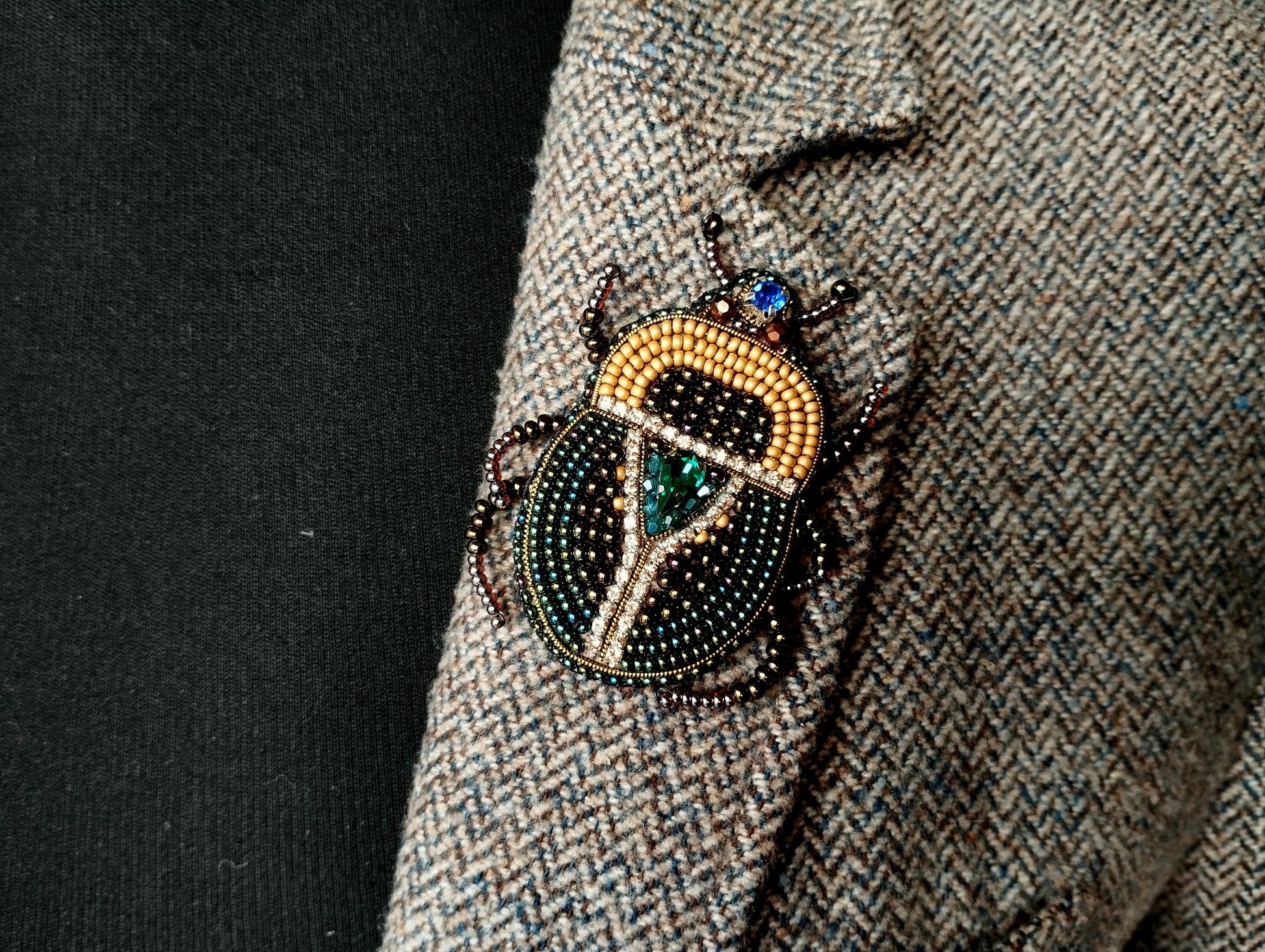 A close-up of a decorative insect brooch on a tweed jacket lapel.