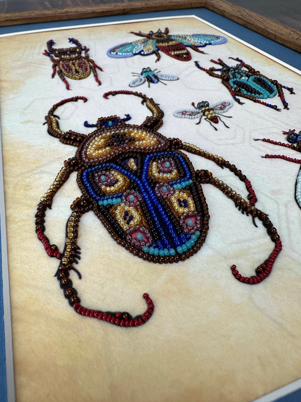 a close-up view of a detailed beaded artwork depicting a large, colorful beetle surrounded by smaller insects.