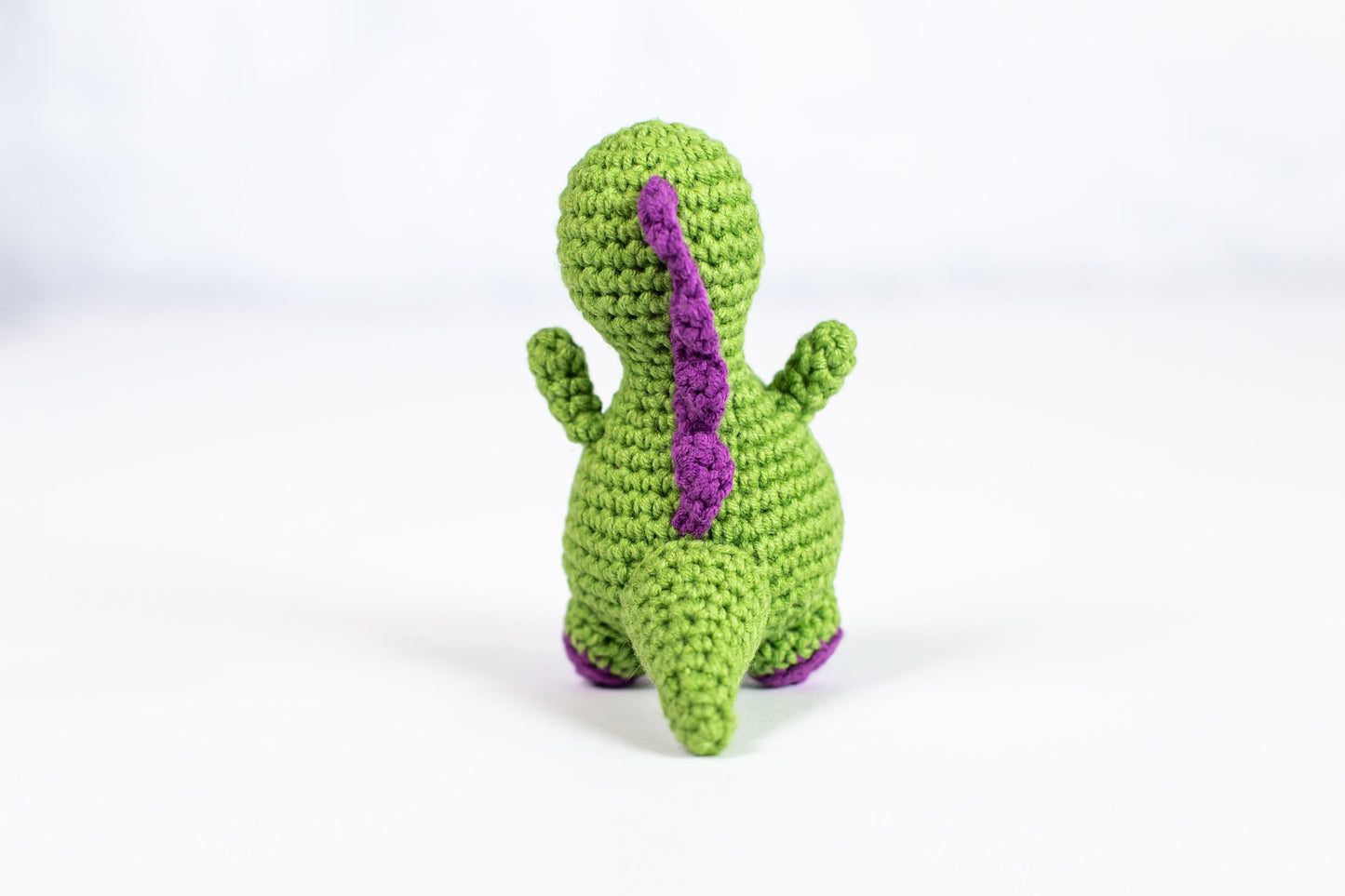 a crocheted toy of a green dinosaur with a purple tail