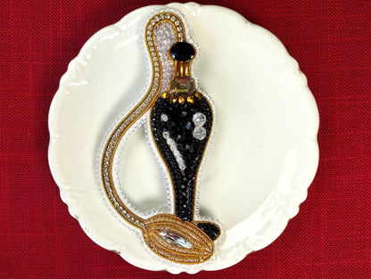 A decorative black perfume bottle with gold accents and rhinestones is displayed on a white plate against a red background.