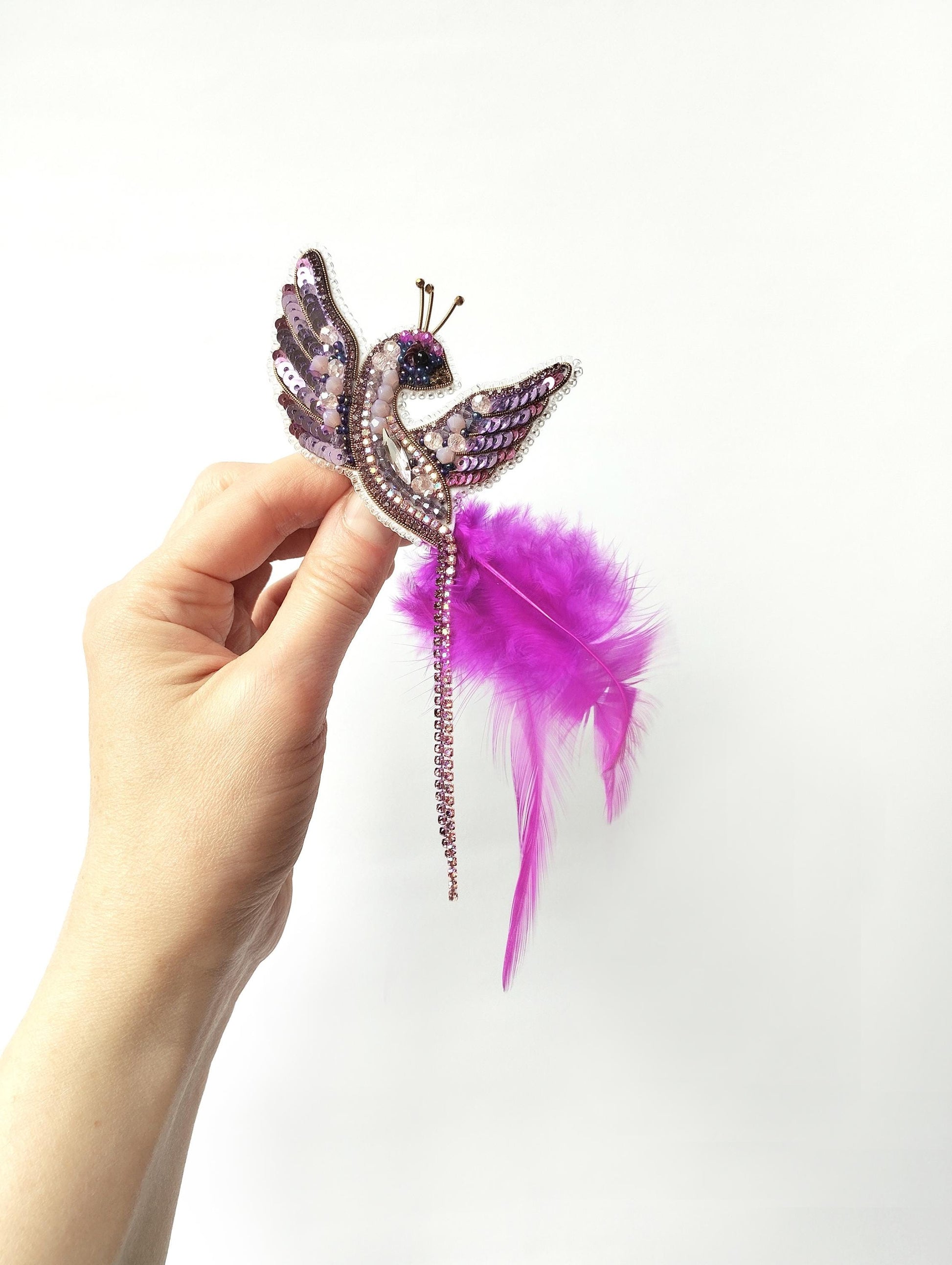 A hand holding a decorative purple and pink feather headband against a white background.
