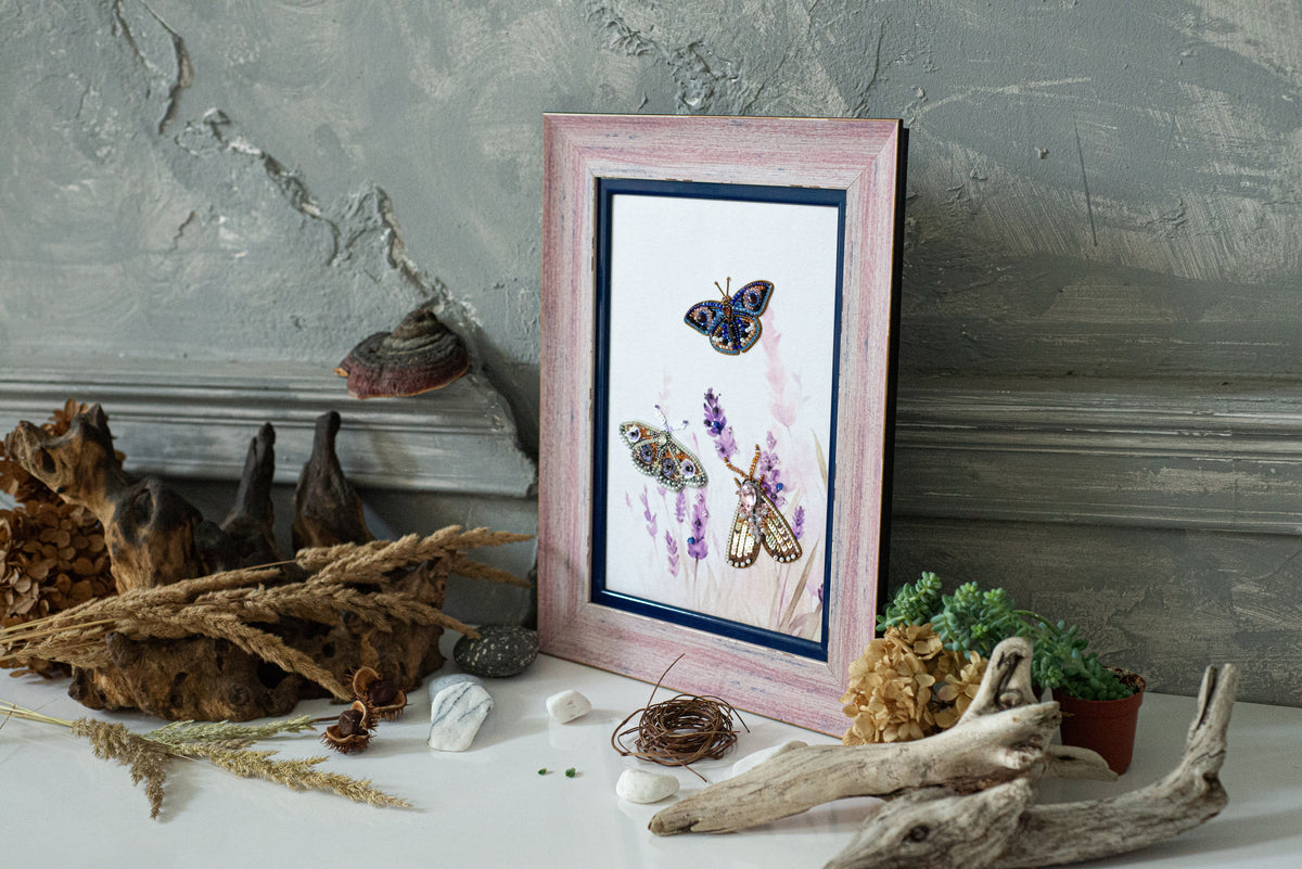 a pink picture frame with a painting of butterflies, surrounded by various natural elements such as driftwood, rocks, and dried flowers.
