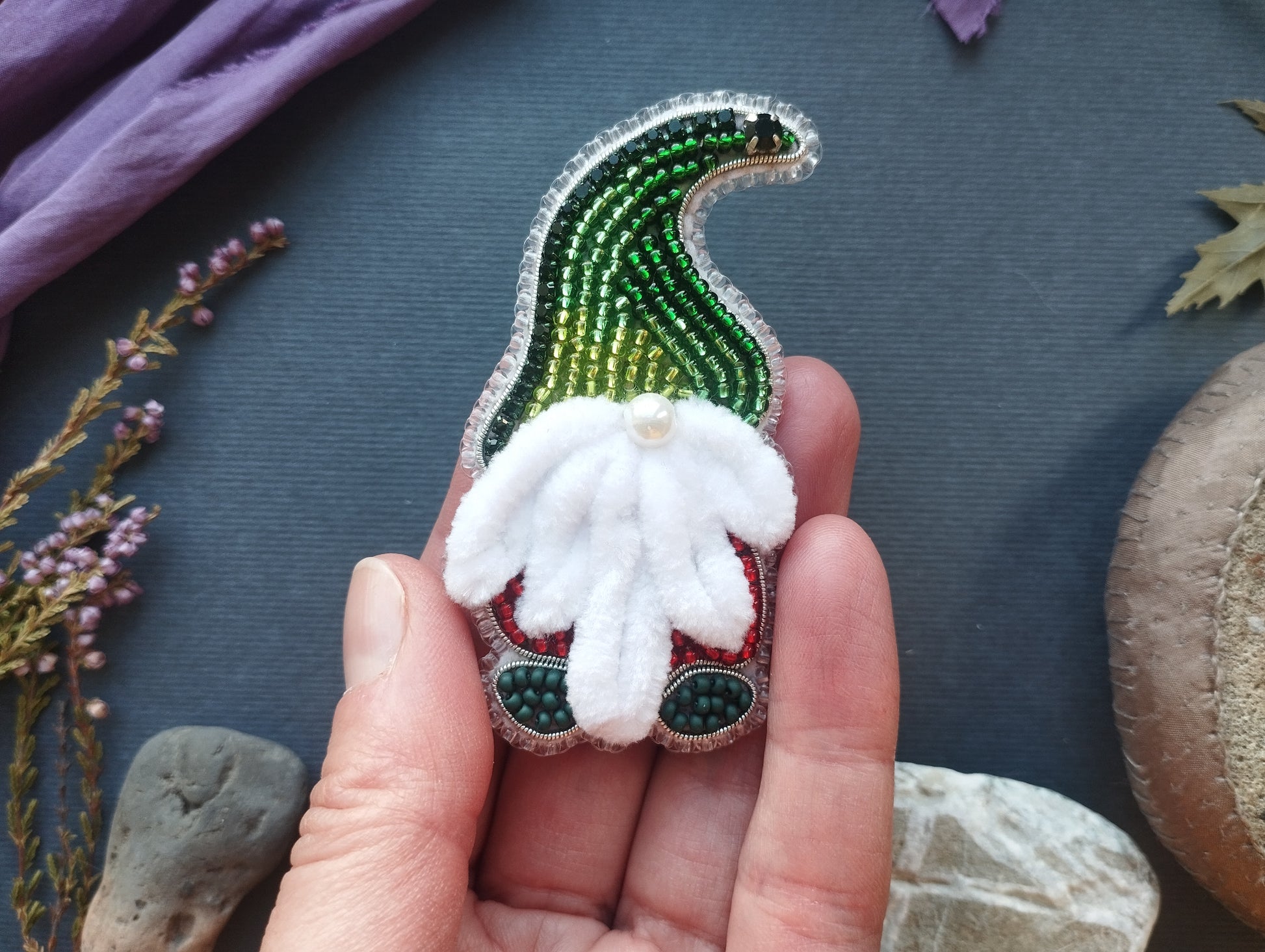 A hand holding a small, intricately designed ornament featuring a gnome-like figure with a white beard and green and red accents.