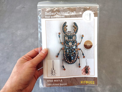 A hand holding a package containing a Stag Beetle embroidery kit.