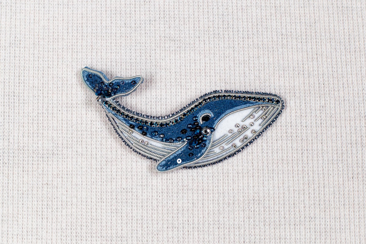 a blue and white embroidered or beaded object resembling a whale, placed on a plain white background.