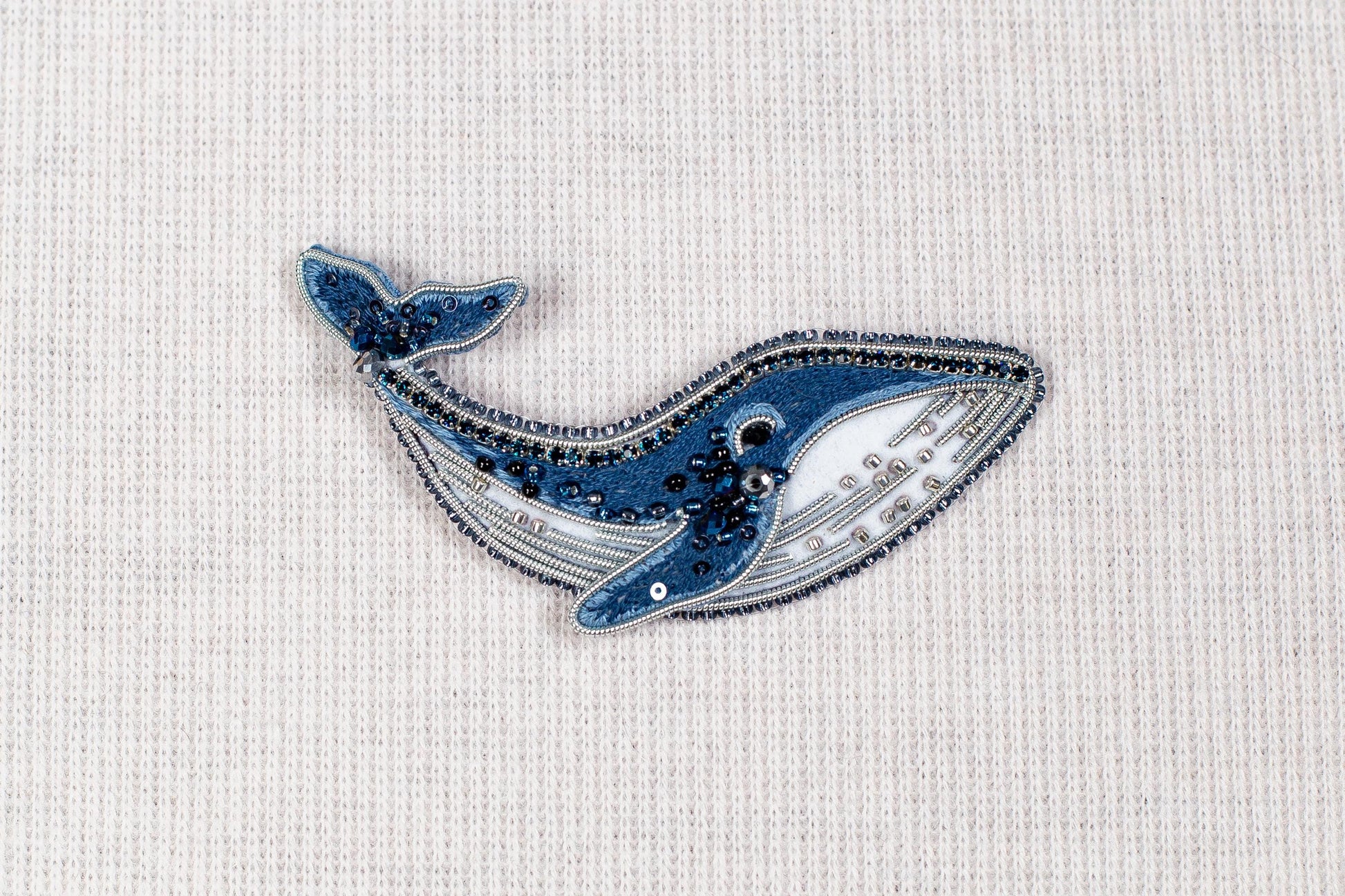 a blue and white embroidered or beaded object resembling a whale, placed on a plain white background.