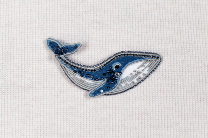 a blue and white embroidered or beaded object resembling a whale, placed on a plain white background.