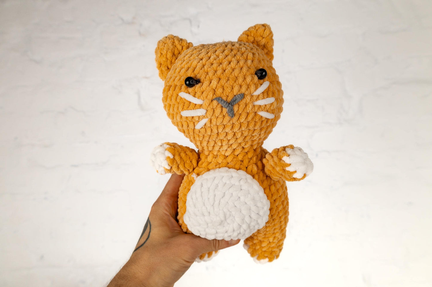 a hand holding a crocheted orange and white cat