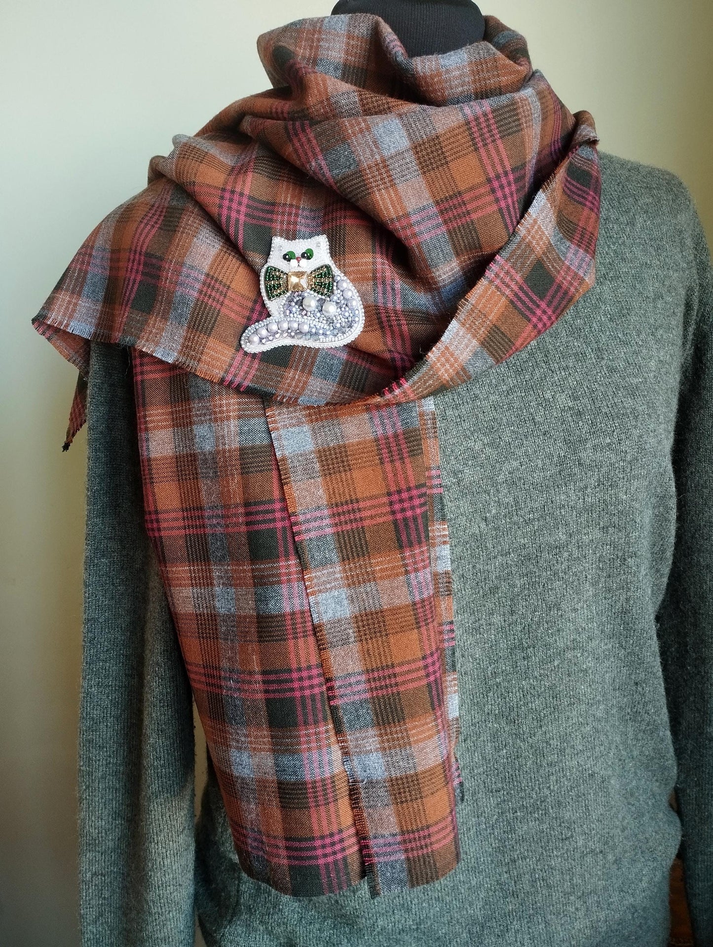 A mannequin wearing a gray sweater and a plaid scarf with a small white owl pin on it.