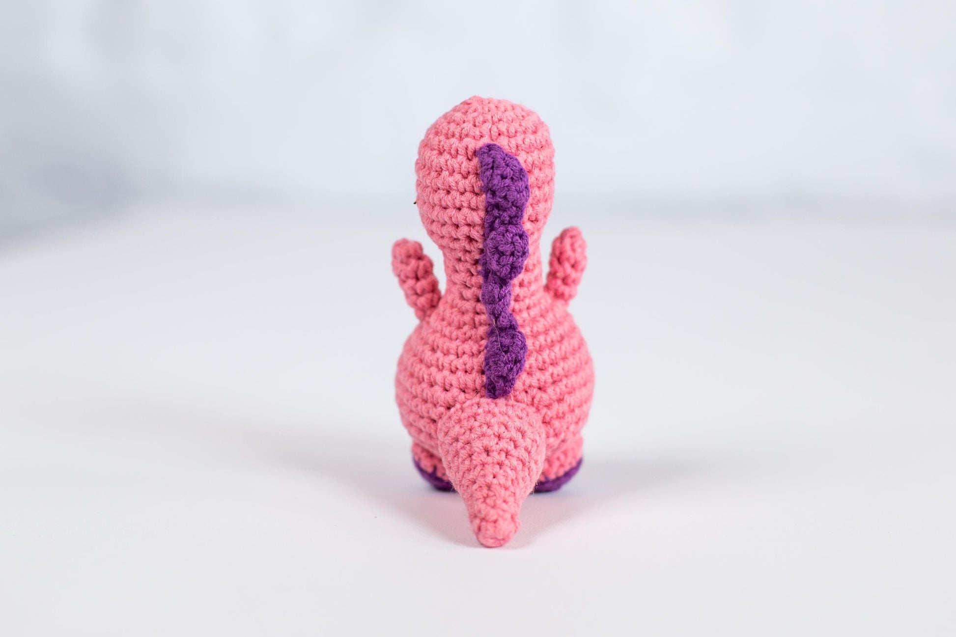 a crocheted pink and purple toy sitting on a white surface