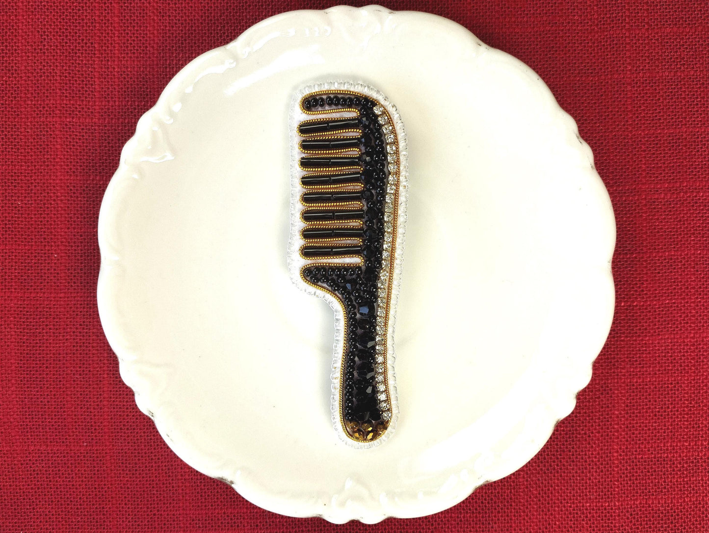 A white plate with a black and gold comb-like object placed on it, set against a red background.
