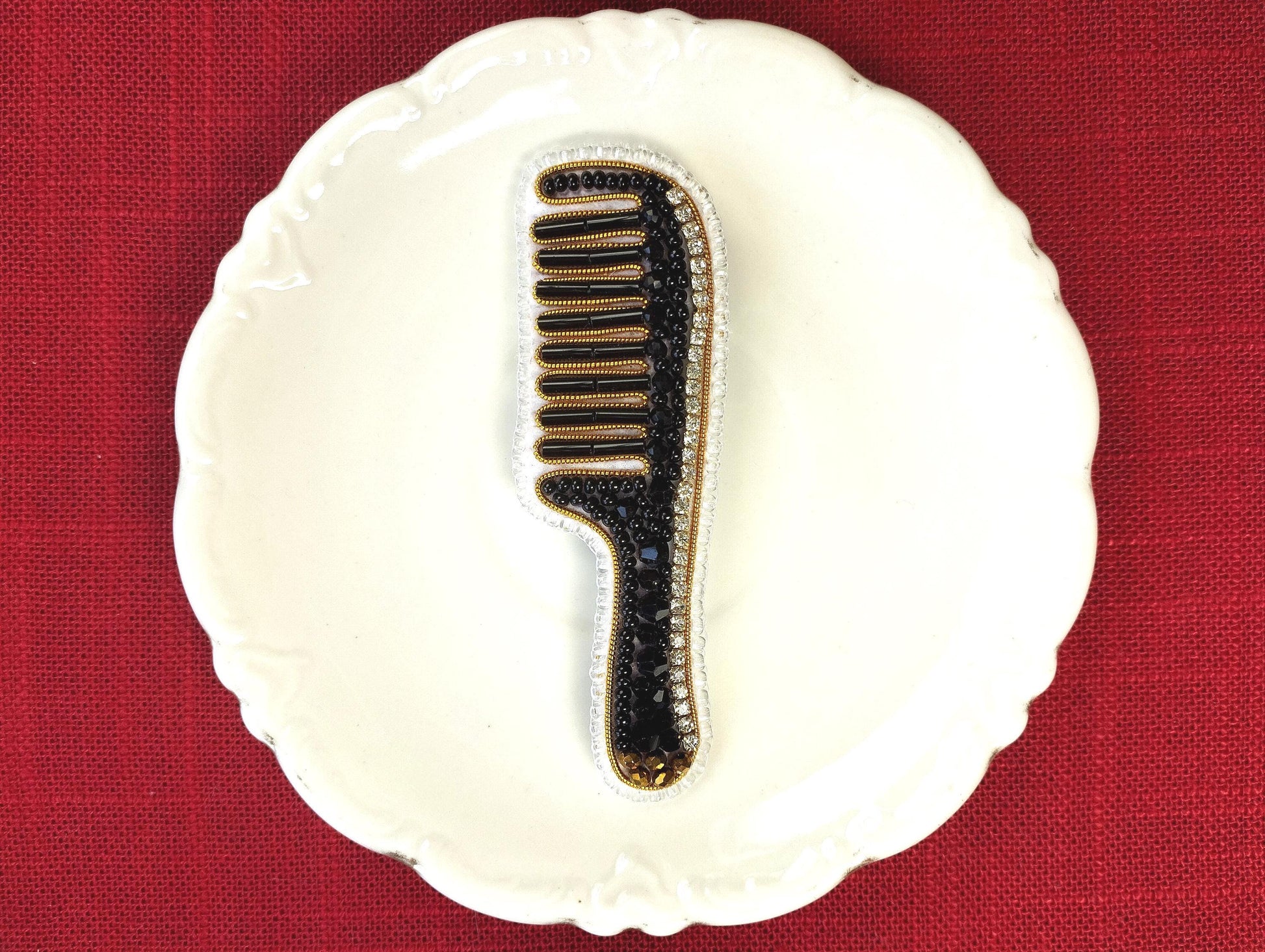 A white plate with a black and gold comb-like object placed on it, set against a red background.