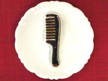 A white plate with a black and gold comb-like object placed on it, set against a red background.