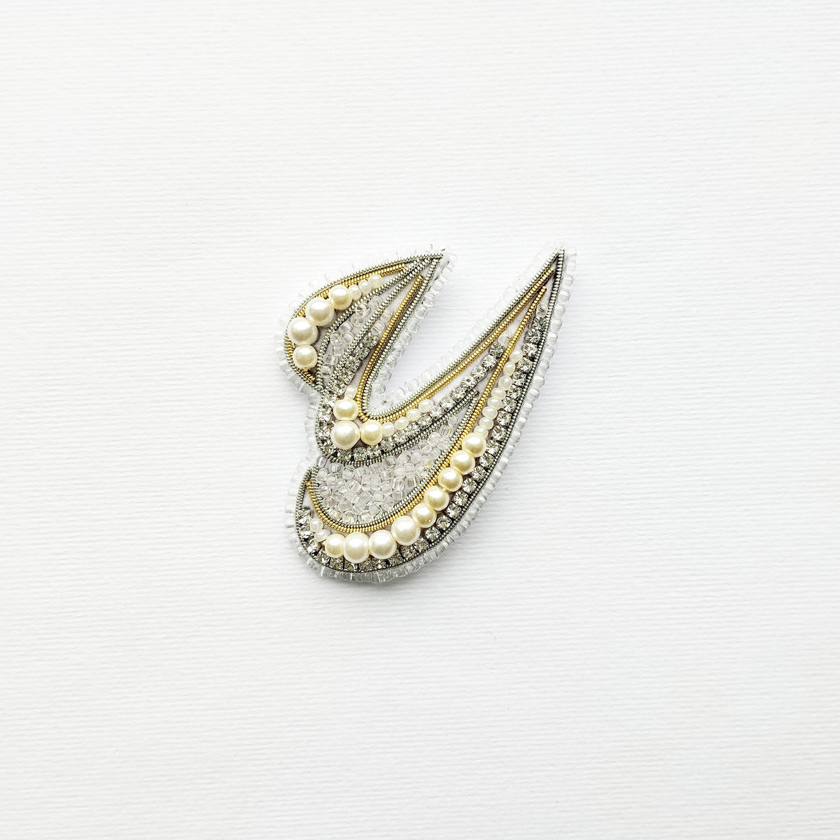 A decorative piece made of pearls and diamonds, featuring a stylized design resembling a letter or symbol.