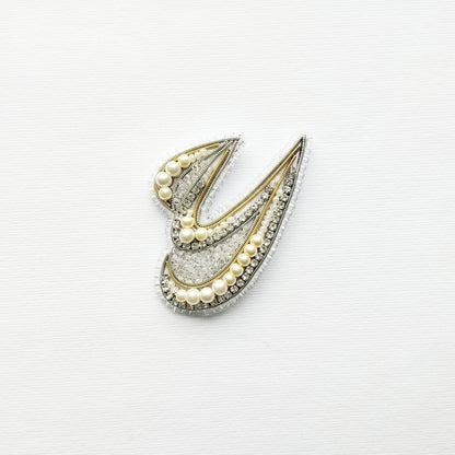 A decorative piece made of pearls and diamonds, featuring a stylized design resembling a letter or symbol.