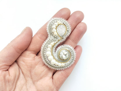 A hand holding a decorative piece of jewelry, which appears to be a brooch or pendant.