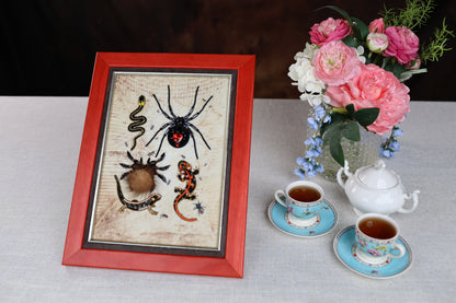 a framed artwork of various insects, including a spider, on a table with a vase of pink flowers and two teacups.