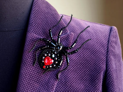 A close-up view of a purple jacket with a black spider-shaped brooch featuring a red heart in the center.