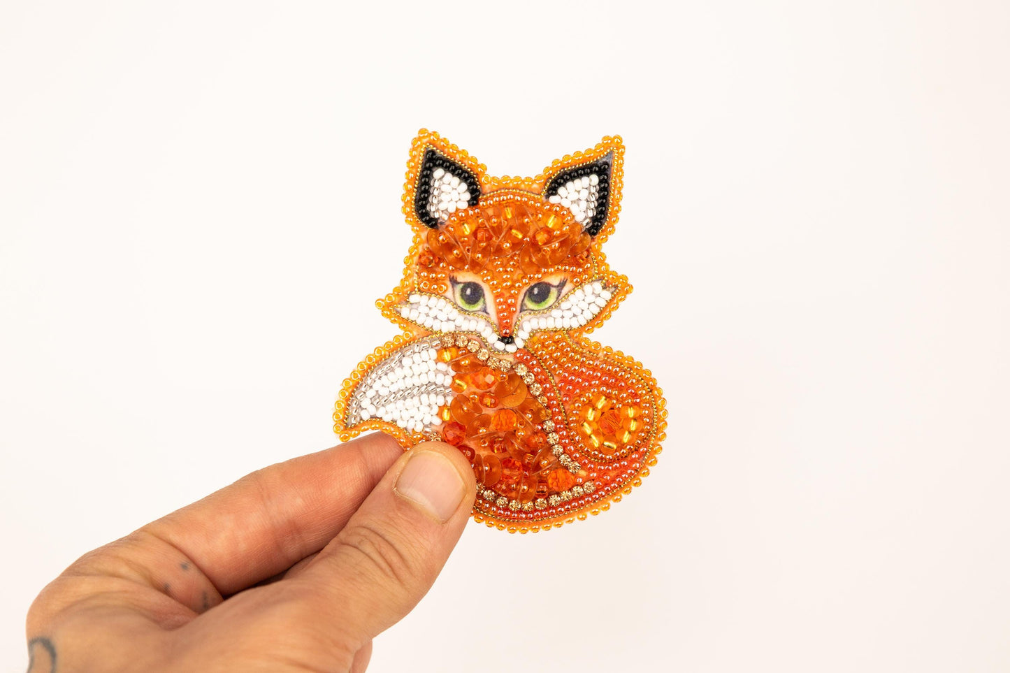 a hand is holding a beaded fox brooch