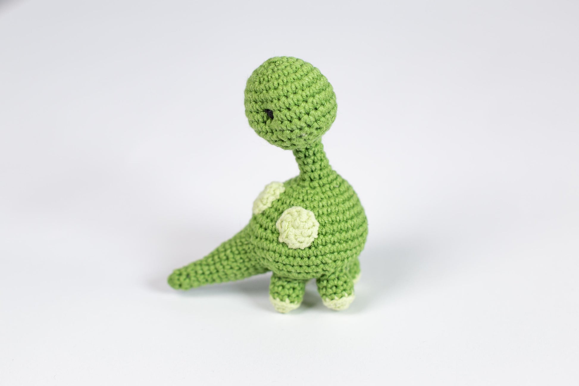 a crocheted green toy dinosaur with a white flower on its chest