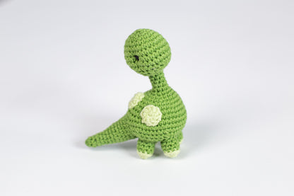 a crocheted green toy dinosaur with a white flower on its chest