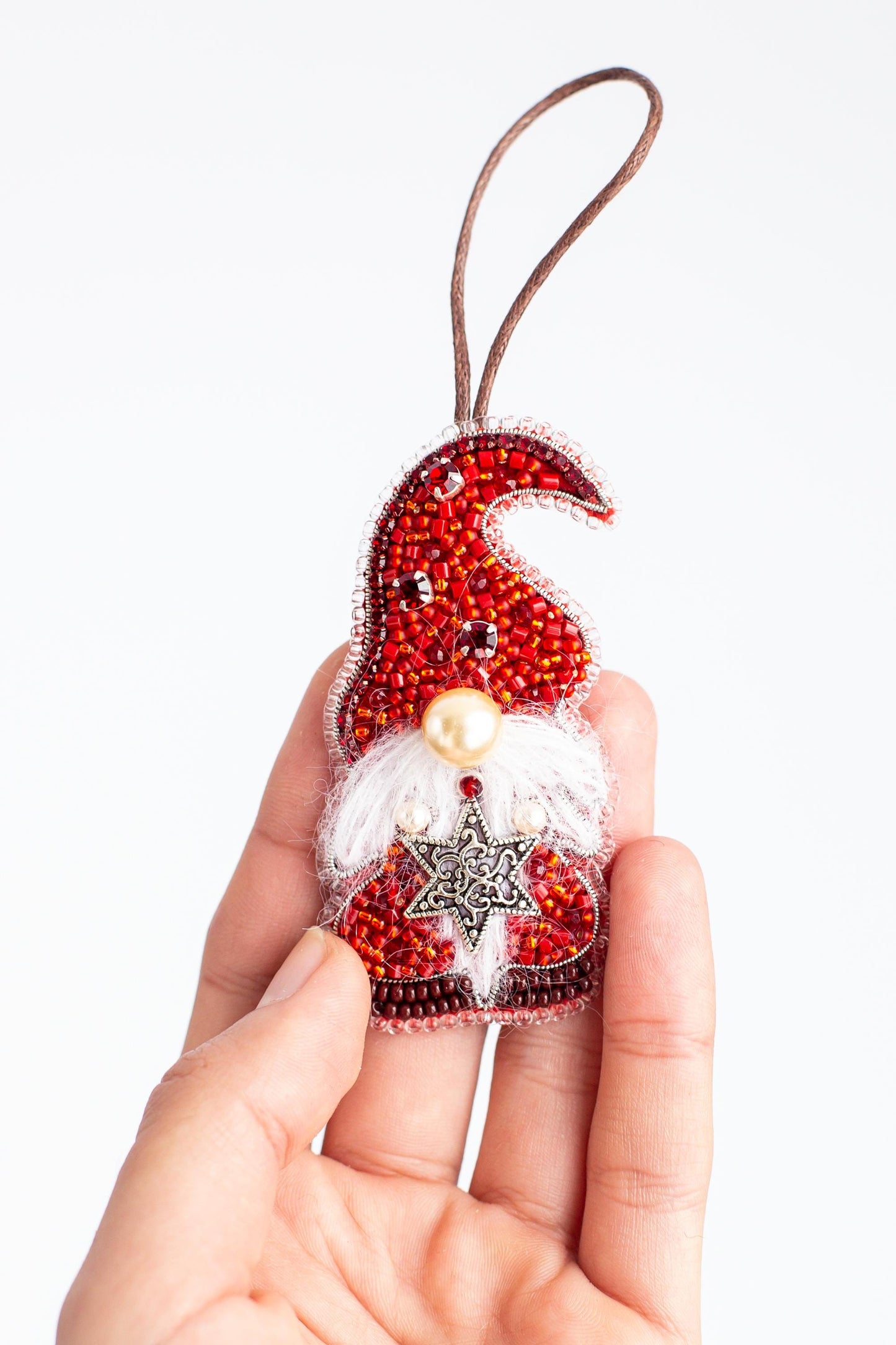 A hand holding a small ornament in the shape of a gnome, which is decorated with red beads and a star.