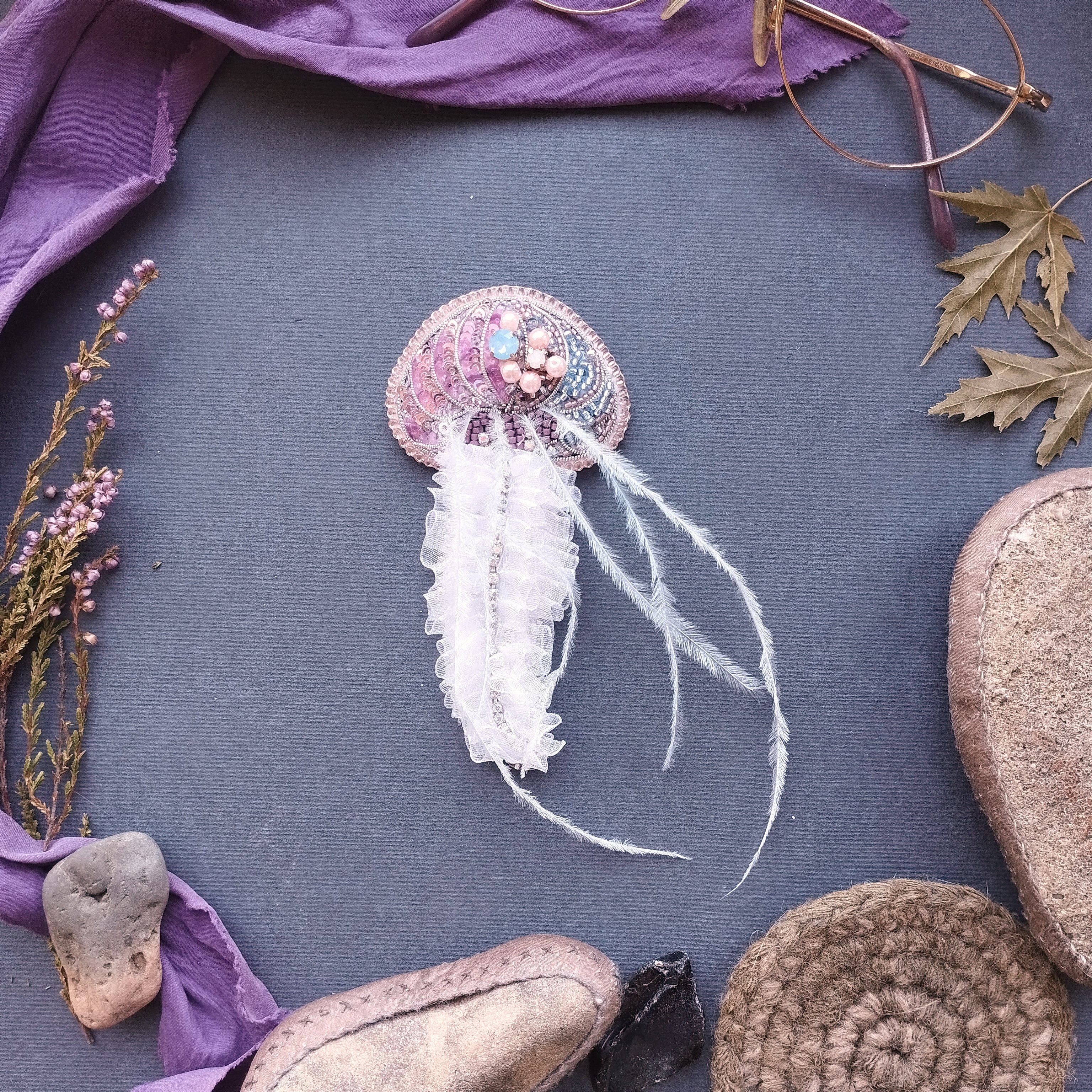 a collection of various objects, including a beaded, ruffled, and feathered piece, surrounded by a purple cloth, leaves, and other natural elements.