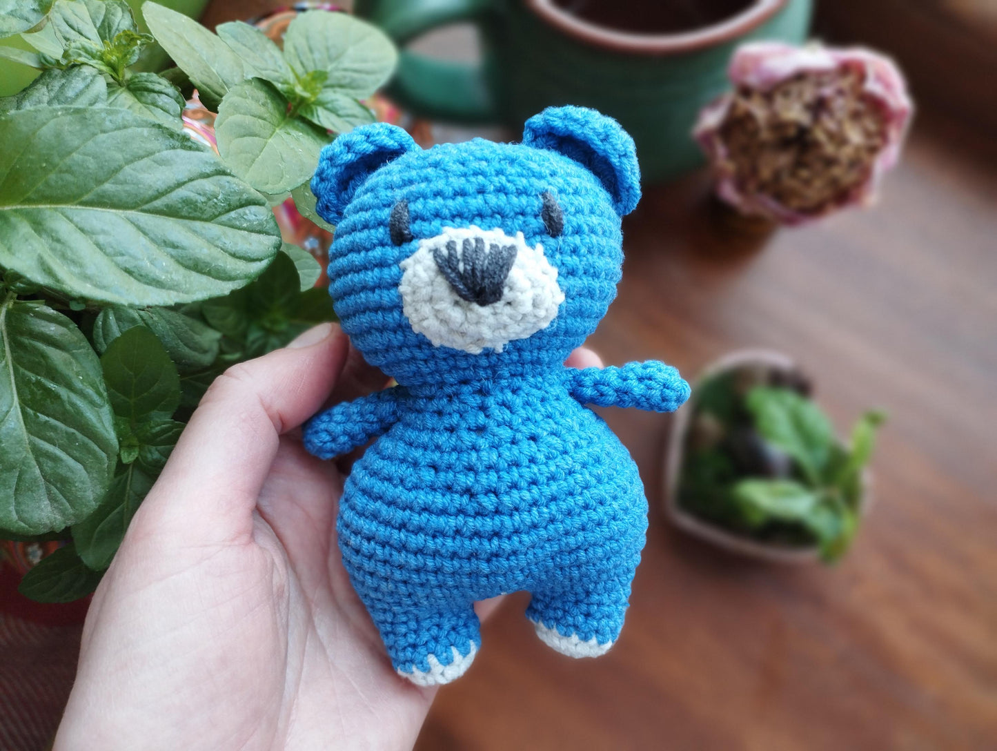 a crocheted blue teddy bear sitting next to a potted plant