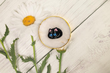 a black cat brooch sitting on top of a white table next to a flower