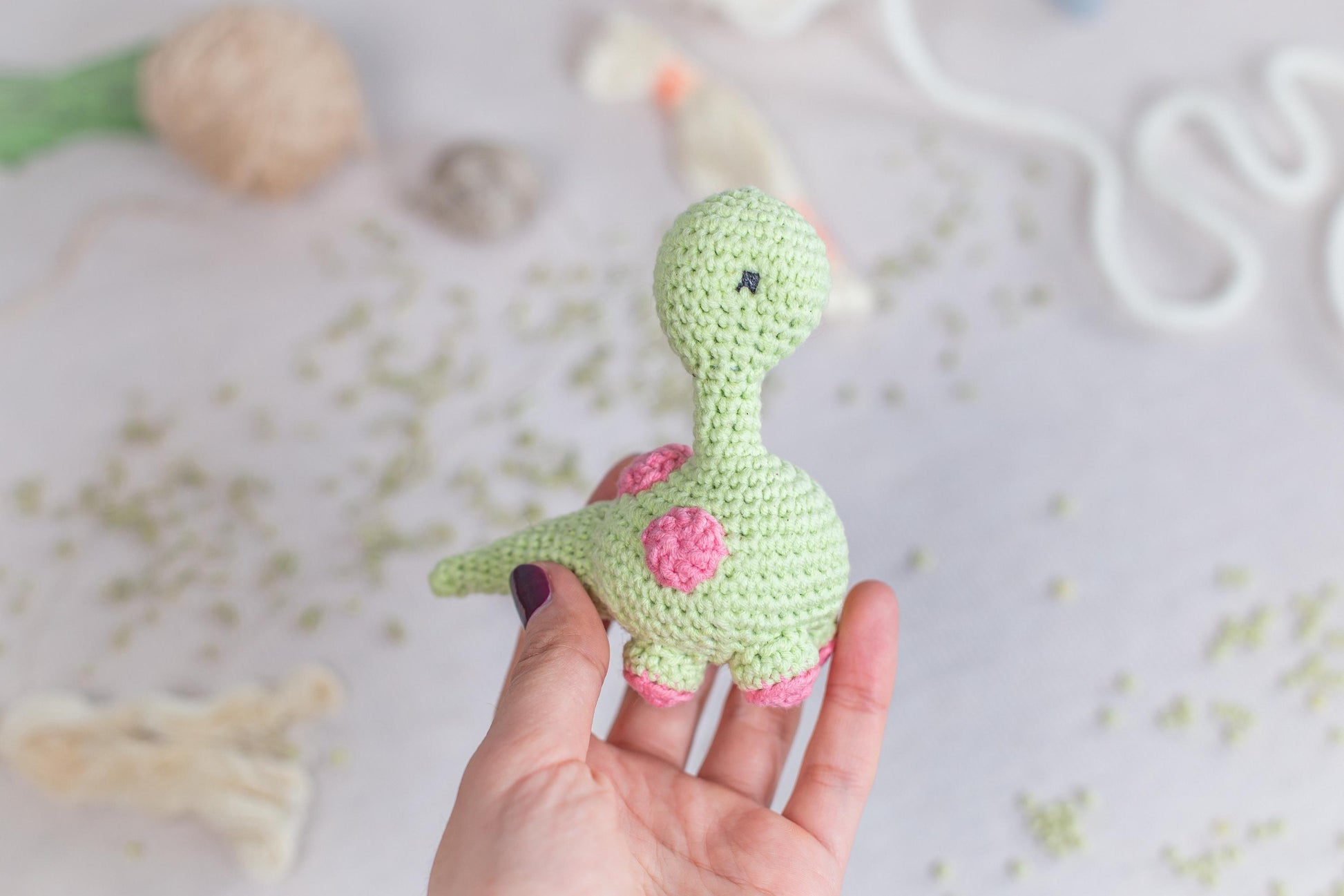 a hand holding a small crocheted toy of a dinosaur