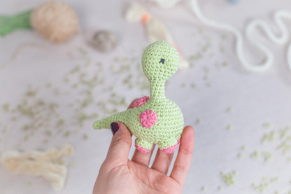 a hand holding a small crocheted toy of a dinosaur