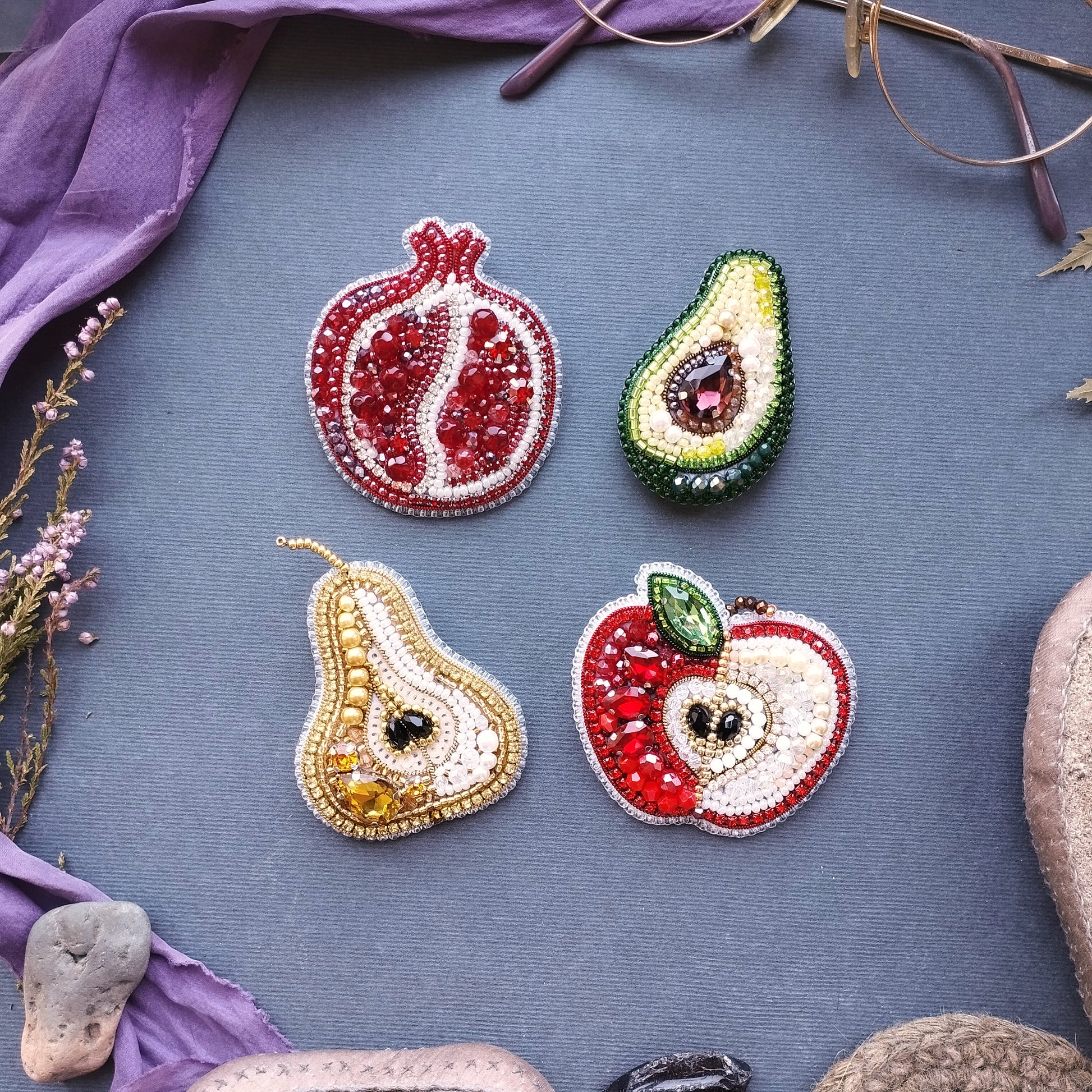 four decorative fruit brooches, each with a unique design and color, arranged on a blue background.