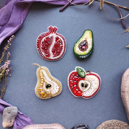 four decorative fruit brooches, each with a unique design and color, arranged on a blue background.