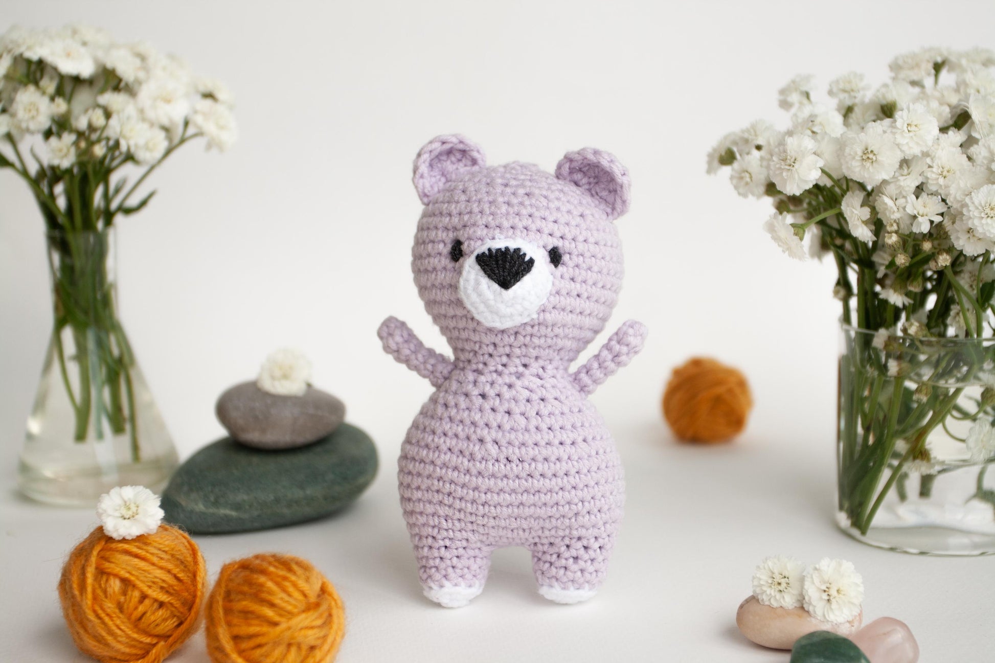 a crocheted teddy bear standing next to a vase of flowers