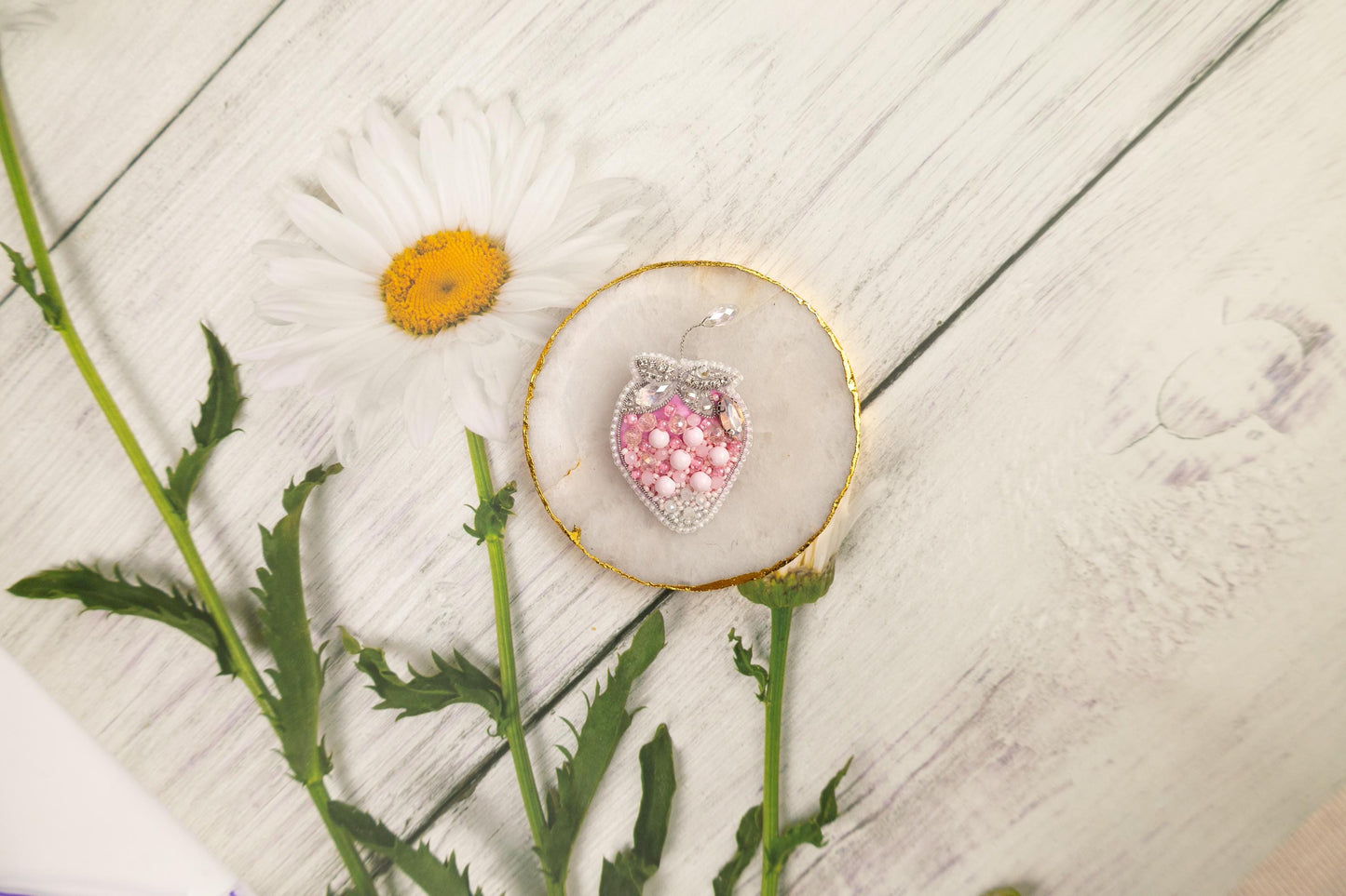a white flower and a pink and white brooch sitting on a white wooden surface