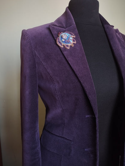 A mannequin wearing a purple velvet jacket with a decorative brooch on the left side.
