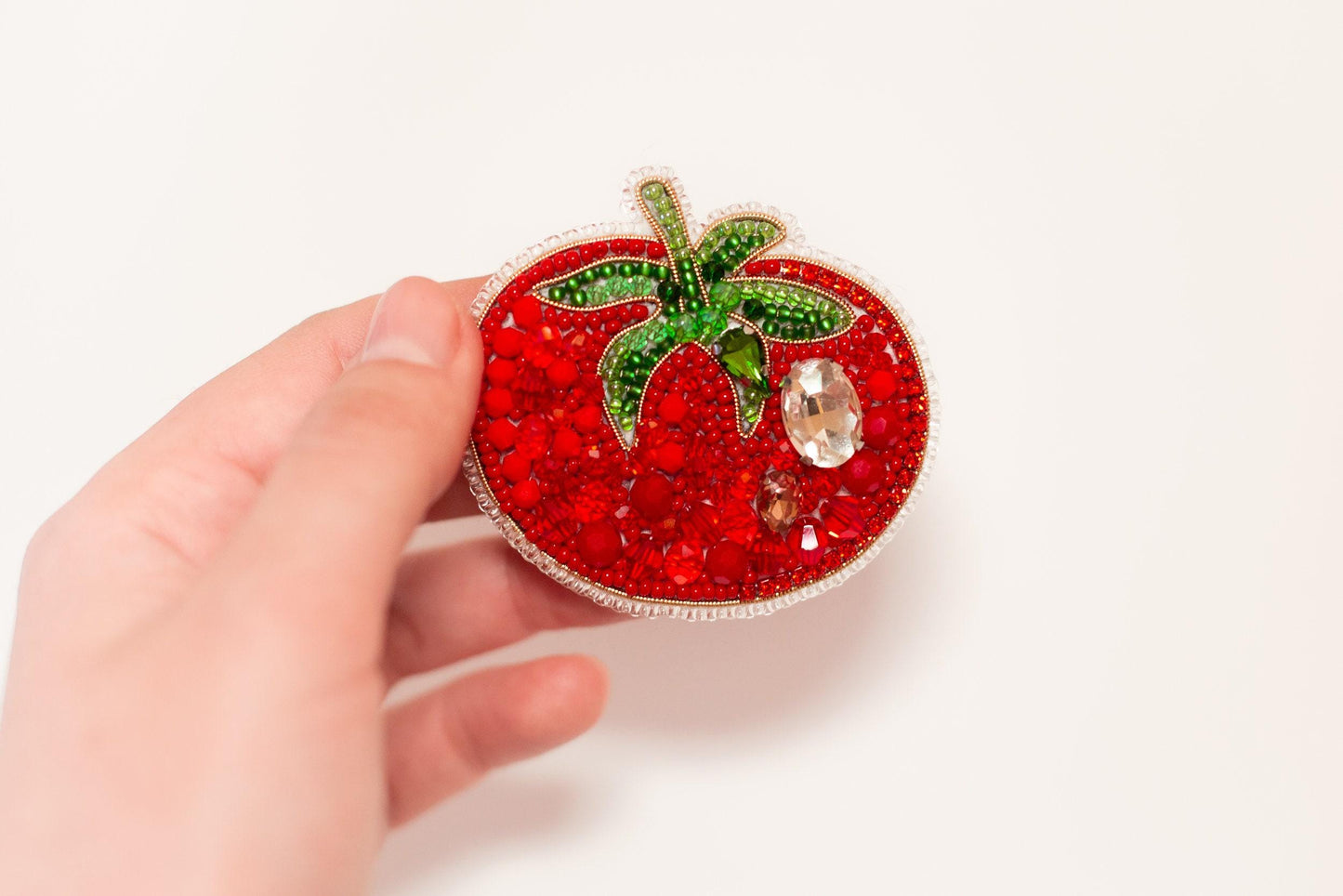 a hand holding a small red strawberry brooch