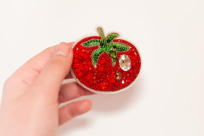 a hand holding a small red strawberry brooch
