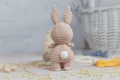 a crocheted bunny standing next to a basket of yarn