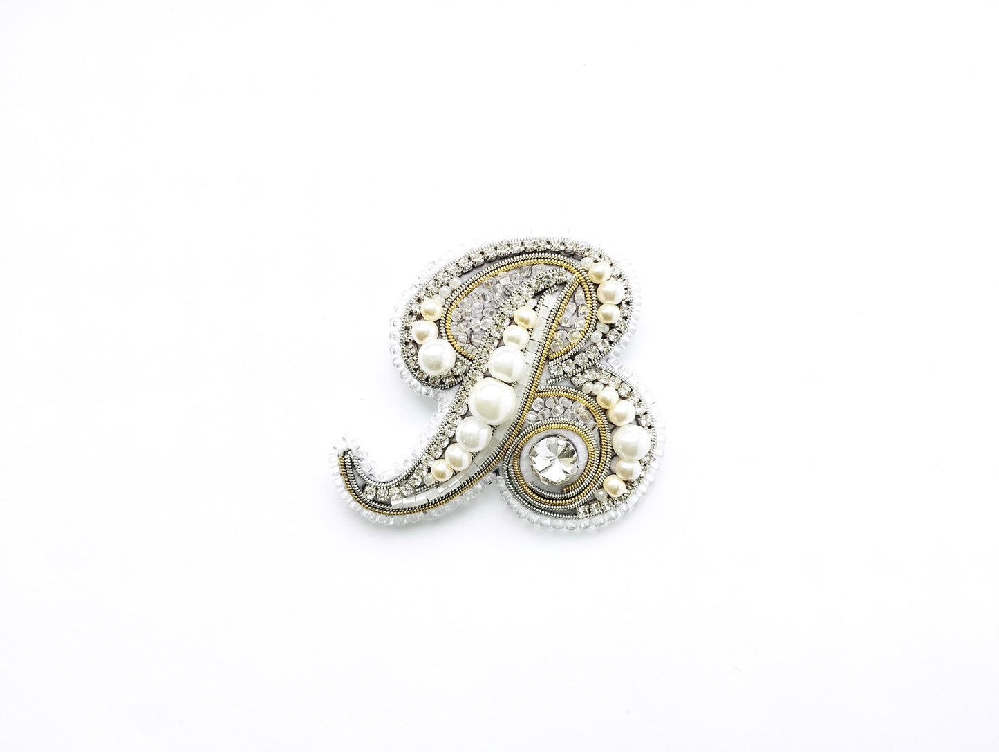 A decorative letter 'B' made of various materials, including pearls, beads, and crystals, against a white background.