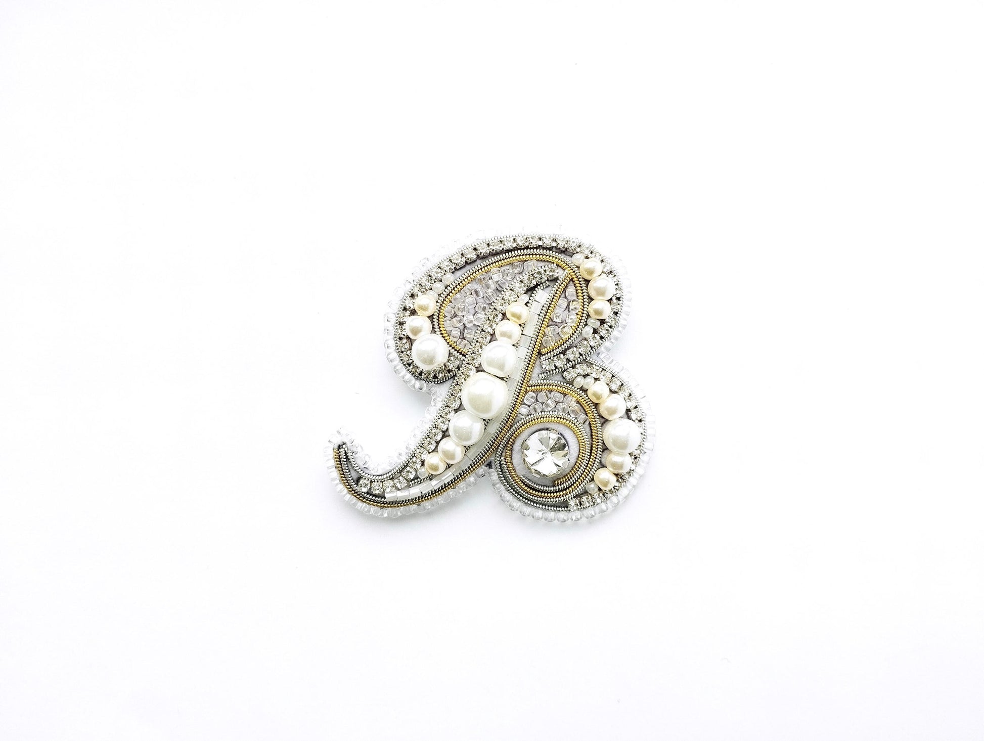 A decorative letter 'B' made of various materials, including pearls, beads, and crystals, against a white background.