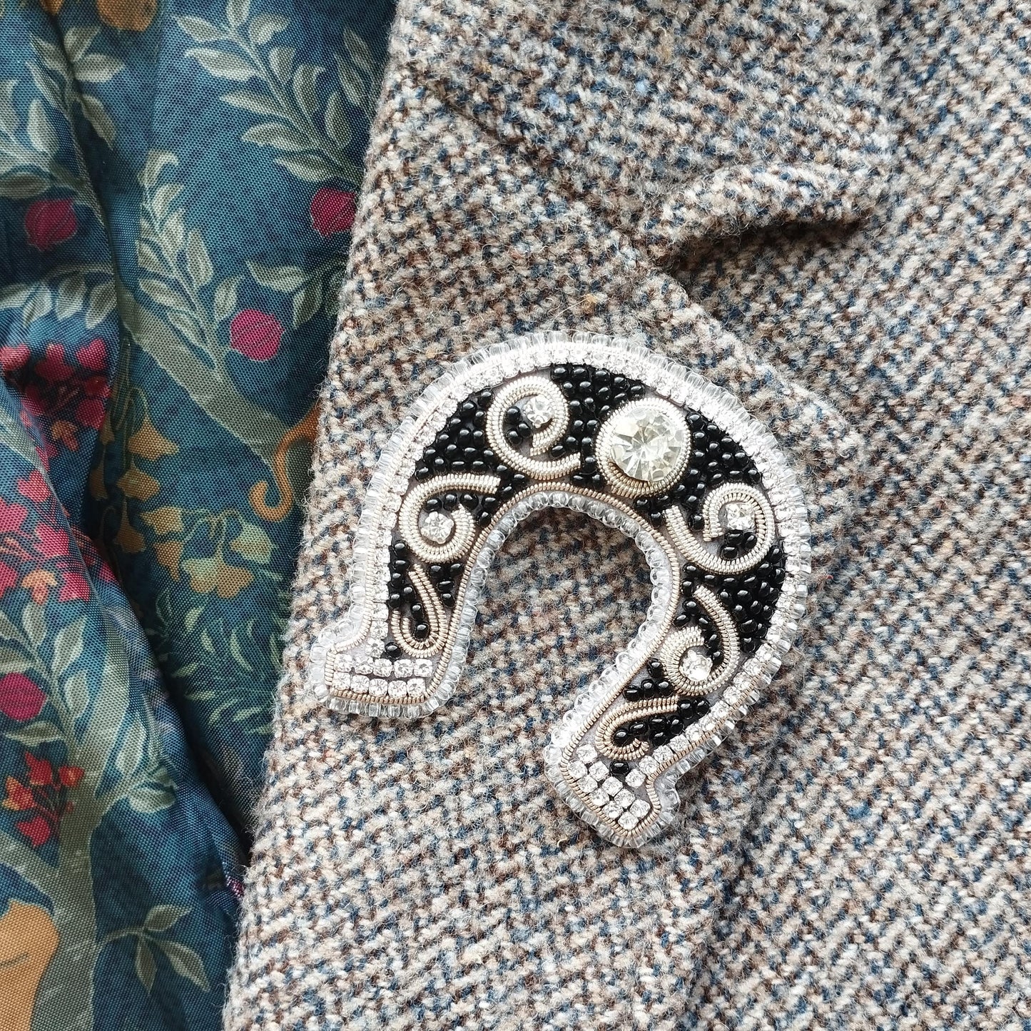 A close-up image of a decorative brooch or pin with a horseshoe-shaped design, placed on a fabric with a floral pattern.