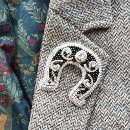 A close-up image of a decorative brooch or pin with a horseshoe-shaped design, placed on a fabric with a floral pattern.