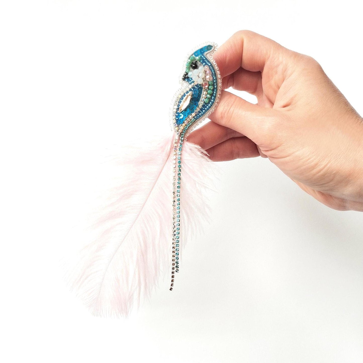 A hand holding a decorative feather earring with a blue and green design.
