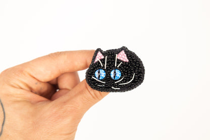 a hand holding a black cat brooch with blue eyes