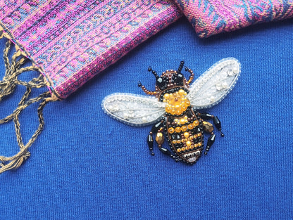 A close-up view of a beaded, embroidered bee pin on a blue fabric surface.