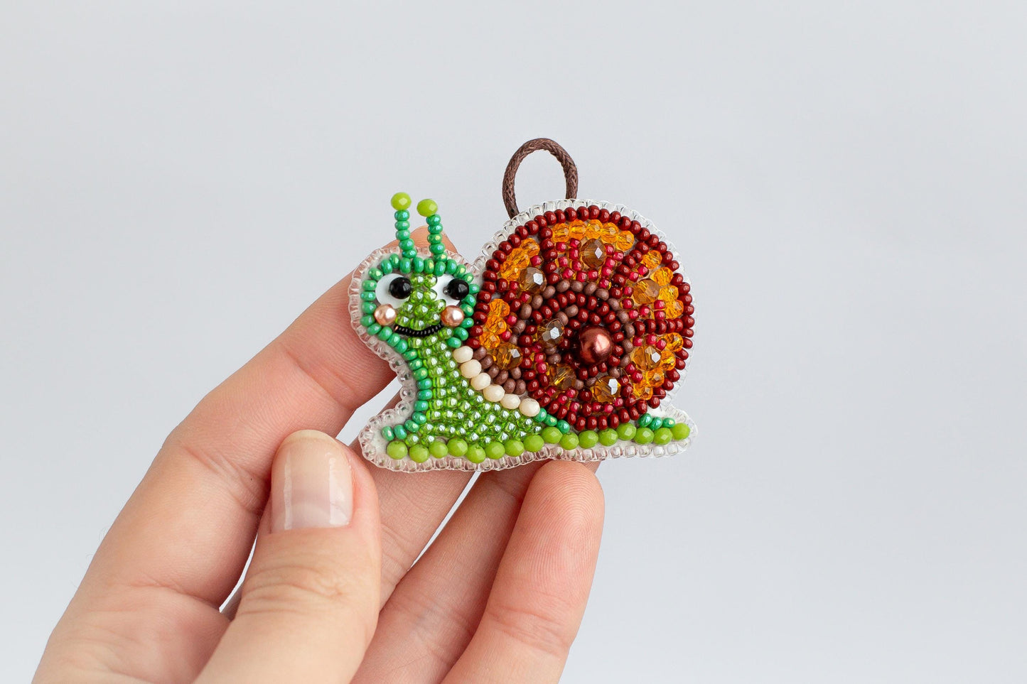 A hand holding a small, colorful beaded ornament shaped like a snail.