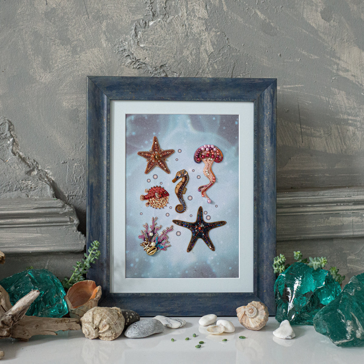 a framed artwork depicting various marine life, including starfish, jellyfish, and coral, set against a blue background. The artwork is surrounded by seashells, rocks, and other natural elements, creating a nautical-themed display.