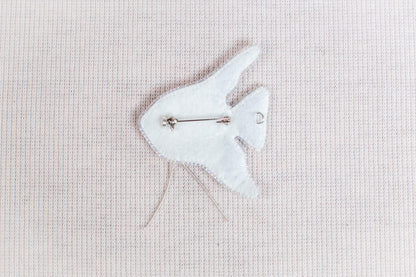 A white felt fish pin is shown against a light pink background.